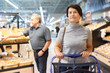 © caftor - Elderly female shopper with a shopping cart chooses groceries in supermarket