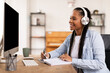 © Prostock-studio - Smiling black female student with headphones taking notes from online lecture