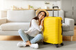 © Prostock-studio - Cheerful young woman sitting on the floor next to vibrant yellow suitcase