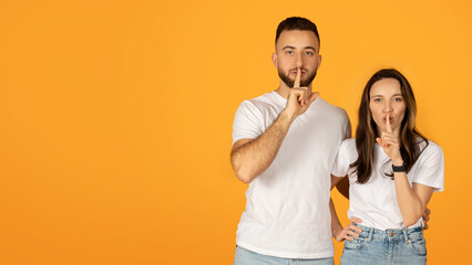 Poster - Quietly confident man and woman in white shirts placing fingers on lips in a 'shush' gesture