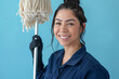 Portrait of a beautiful smiling cleaner with a mop in her hands on a coloured background in work clothes