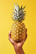 Female hand holding ripe pineapple on isolated bright yellow background with copy space. Close up. Concept of natural healthy food or tropical summer juicy fruits. Minimalism.