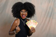 © Edson Souza - A black woman holds up Brazilian money, smiles, looks at the camera and celebrates with her hand.