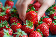 A Hand Grabbing A Strawberry From A Pile On The Table