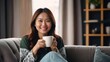 Asian woman drinking coffee sitting on sofa at home