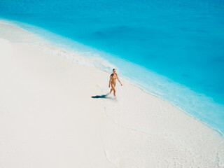 Wall Mural - Woman in swimsuit walking on tropical white sandy beach with turquoise ocean water. Aerial view