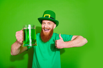 Wall Mural - Photo of cheerful handsome guy hold beer cocktail mug show thumb up approve isolated on green color background