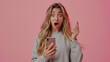 A startled woman with wide eyes and an open mouth is holding a smartphone, gesturing with one hand as if reacting to surprising news.