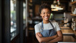 Smiling woman small business owner in apron standing confidently in front of a cafe, with warm lighting and blurred interior details in the background.