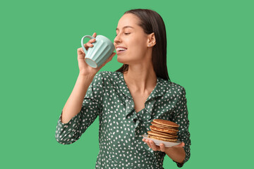 Poster - Beautiful young woman with tasty pancakes and cup of tea on green background