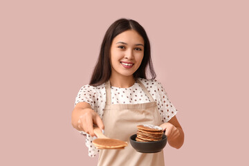 Sticker - Young Asian woman holding frying pan with tasty pancakes on pink background