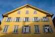 Untersicht historisches Gebäude mit Fensterladen und Sprossenfenstern vor blauem Himmel.