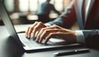 © ZeNDaY - Close up of a business professional's hands typing on a laptop keyboard with colleagues in discussion in the background.
