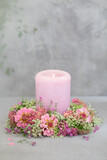 Różowa świeca otoczona wiankiem z letnich kwiatów. Cynie.