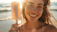 a woman holding a popsicle on a beach with the sun shining on her face and smiling at the camera