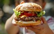 A close-up of a child's hand holding a huge burger, focusing on unbalanced nutrition. Сildhood obesity problem