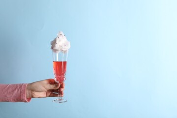 Sticker - Woman holding glass of cotton candy cocktail on light blue background, closeup. Space for text