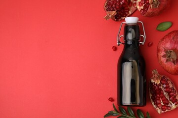 Wall Mural - tasty pomegranate sauce in bottle, leaves and fruits on red background, flat lay. space for text