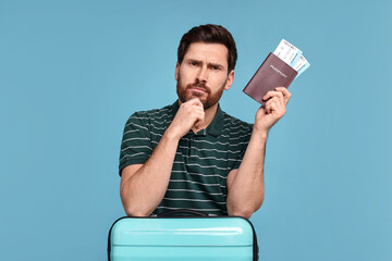 Wall Mural - Thoughtful man with passport, suitcase and tickets on light blue background