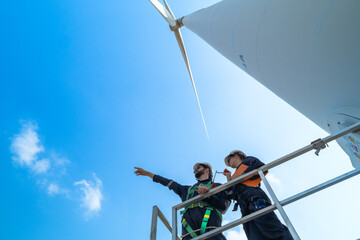 uprisen angle engineers working in fieldwork at outdoor with wind turbine and clear sky. Workers check construction. Wind turbines for electrical clean energy and environment sustainability.