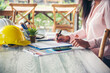 © aFotostock - Civil construction engineer woman working with laptop at desk office white, yellow safety hard hat in construction site office. Asian young man architecture project manager sitting at office on site