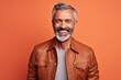 Smiling mature man in leather jacket. Portrait of cheerful mature man in leather jacket looking at camera and smiling while standing against orange background