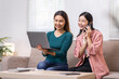 © David - Two Asian women communicate with their friends and classmates via video link using a laptop and smartphone in the living room. Friends, friendship, happy time together