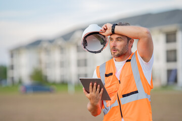 Wall Mural - Portrait of tired builder man. Construction worker with hardhat helmet on construction site. Construction engineer worker in builder uniform. Worker construction.