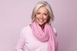 Portrait of a happy senior woman with pink scarf over pink background.