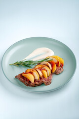 Wall Mural - Steak with chopped apples and cinnamon in a blue plate on a white background. Festive dish with duck