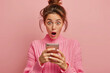 a woman looks at mobile phone with surprised open mouthed expression 
