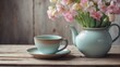 A soft blue teapot and matching cup alongside vibrant pink tulips on a wooden surface