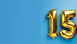 © Uuganbayar - Banner with number 15 golden balloon with copy space. Fifteen years anniversary celebration concept on a blue background.