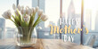 © Maria Shchipakina - White tulips in a vase on a table, 'Happy Mother's Day' text overlaid with cityscape backdrop.