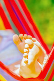 Fototapeta Natura - Close up young beautiful girl sleeping in a hammock with bare feet, relaxing and enjoying a lovely sunny summer day. Safety and happy childhood and leisure concept. Vertical image.