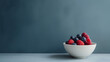 A white bowl is filled to the brim with a colorful assortment of ripe raspberries and plump blueberries