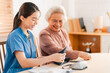 © chokniti - Medical health insurance service, Asian caregiver doctor examine older patient use blood pressure gauge. Young woman therapist nurse nursing home taking care to senior elderly woman