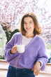 Spring portrait of happy beautiful woman drinking tea or coffee on balcony