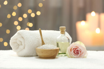 Beautiful spa composition with essential oil, sea salt and rose on white towel against blurred lights