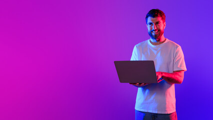 Young caucasian guy using laptop in studio with neon light