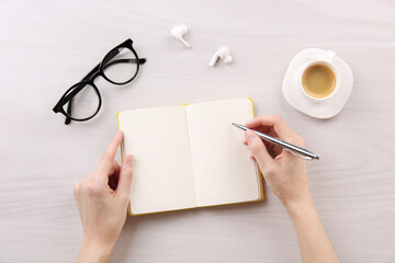 Canvas Print - Woman with notebook and pen at white wooden table, top view. Space for text