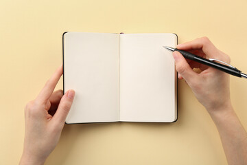 Canvas Print - Woman writing in notebook on beige background, top view