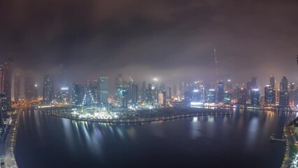 Poster - Aerial panorama of Dubai Business Bay and Downtown during all night with the various skyscrapers and towers along waterfront on canal night timelapse. Construction site with cranes covered by fog