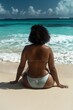 Tranquil african american woman in bikini sitting by the shoreline on a pristine tropical beach