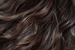 A close up capturing the intricate details of dark brown hair, cascading in soft waves with hints of light bouncing off its surface