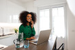 © Mia_Bon - An africano woman cheerfully calling over the phone at home while working with her laptop and water beside her in her home office