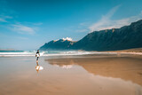 Fototapeta  - surfista si specchia su spiaggia in riva all'oceano sotto la scogliera