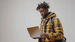 © Favio - 20s African american man wearing a yellow jacket  holding a laptop. Focused on the screen, on white background. Concept of productivity and concentration