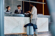 © Drazen - African American man showing his room reservation on smart phone while talking to receptionists at hotel front desk.
