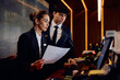 © Drazen - Two receptionists working on computer while checking documents at hotel reception desk.